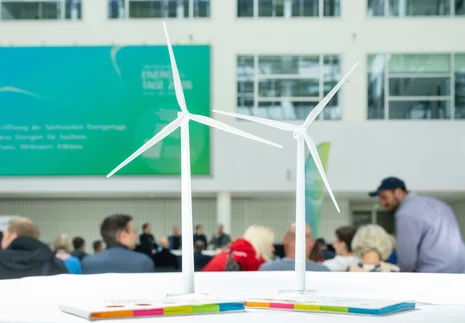 Zwei Windradmodelle mit Zuhörerinnen und Zuhörern einer Veranstaltung im Hintergrund